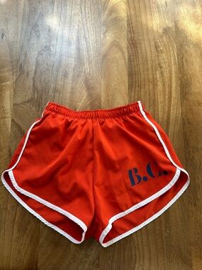 Bobo Choses Red Swim Trunks with navy B.C. logo on bottom left leg